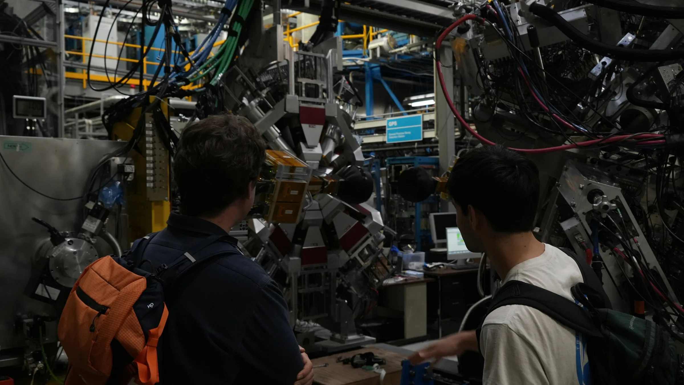 Two people standing in front of a large scientific instrument, looking up into it.